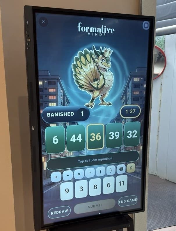 A portrait touchscreen at a tuition centre, showing a Math Attack battle: a monster, five green target cards, a number keypad and five white number cards.